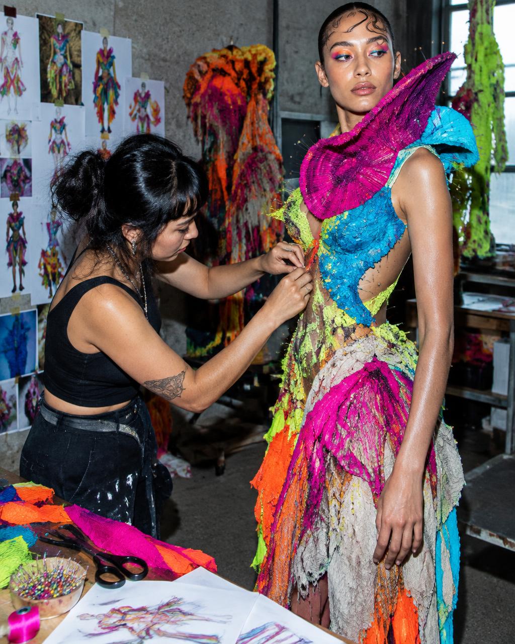 Fashion designer fitting a vivid sculptural garment on a model